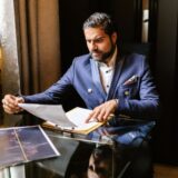 Antreprenor care analizează documente financiare și grafice pe un birou, alături de un laptop și un calculator